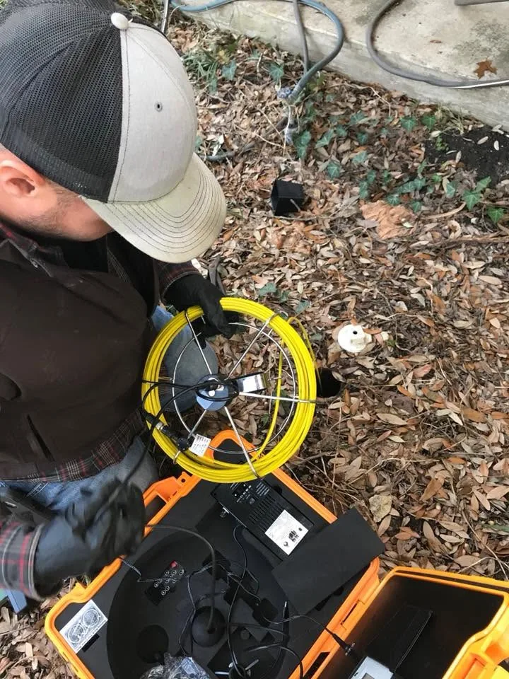 Plumber holding yellow pipe inspection camera equipment at outdoor job site.