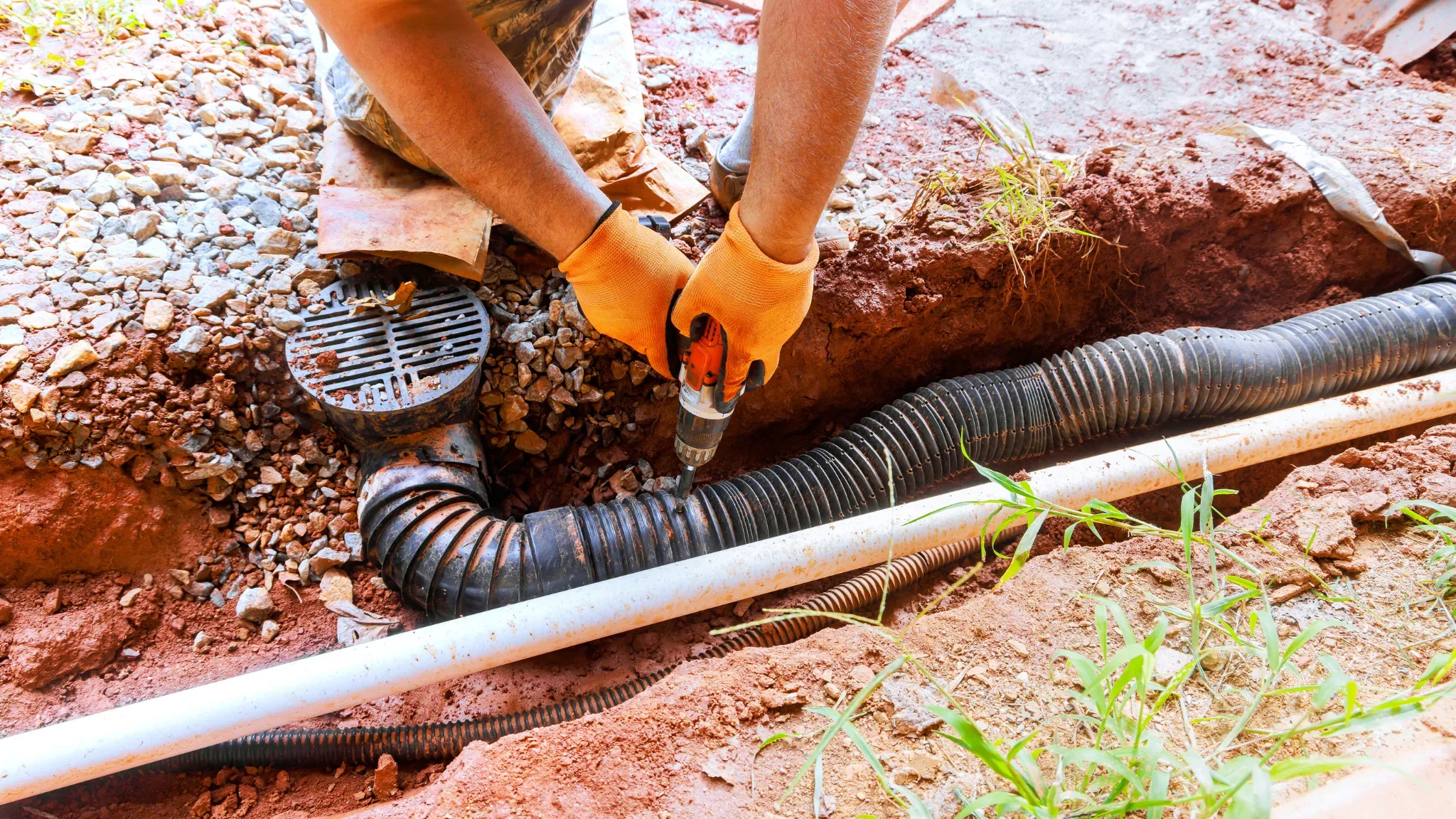 Professional plumber in orange work gloves installing corrugated drainage pipes and fittings in an outdoor residential excava